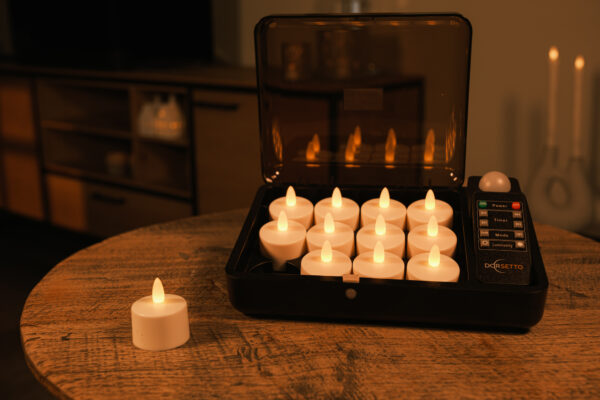 Ein Set von 12 warmweißen, wasserdichten, wiederaufladbaren LED-Wachs-/Teelichtern (Brenndauer 175h) mit Fernbedienung - eines auf einem Holztisch, andere in der schwarzen Ladestation - leuchtet sanft im Raum.