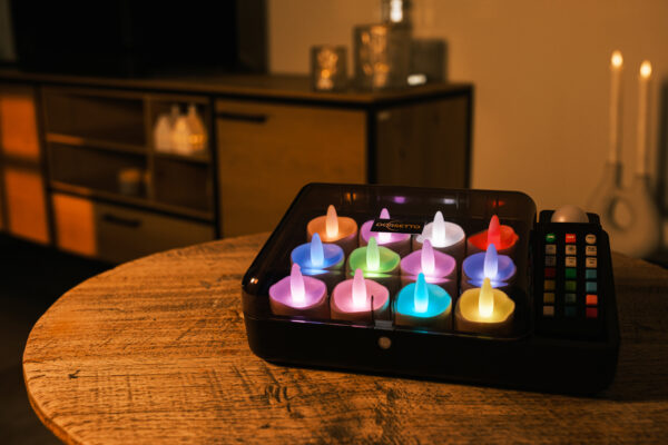 Twaalf RGB LED-was/theelichtjes (oplaadbaar, waterdicht) met afstandsbediening creëren een gezellige sfeer op een houten tafel bij een kast, hun kleurrijke lichtjes gloeien op de achtergrond.