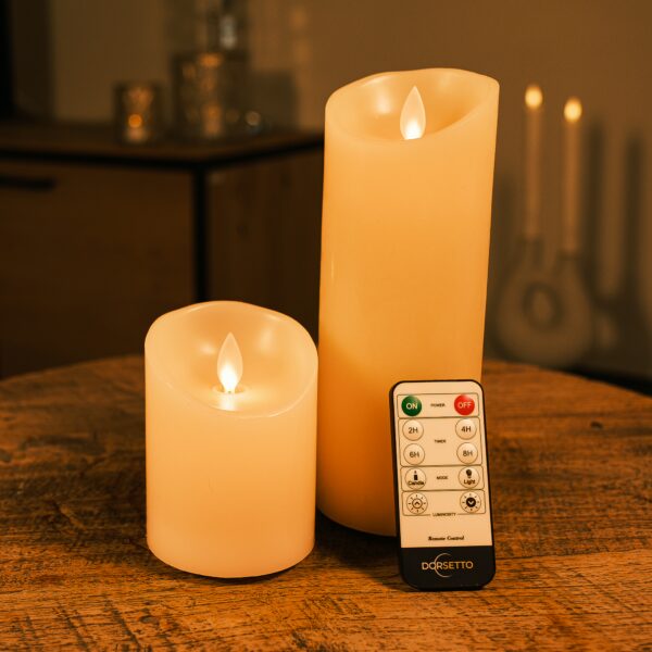 Een set van twee oplaadbare LED-waskaarsen van DORSETTO, een hoge en een korte, staan op een houten tafel met een afstandsbediening met Dorset-label ervoor en een zacht verlichte, onscherpe achtergrond.