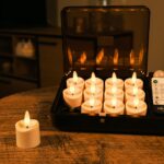 Ein Set von zwölf flammenlosen LED-Teelichtern in einer schwarzen Aufbewahrungsbox mit Fernbedienung, die auf einem Holztisch steht. Ein zusätzliches Teelicht befindet sich außerhalb des Koffers.