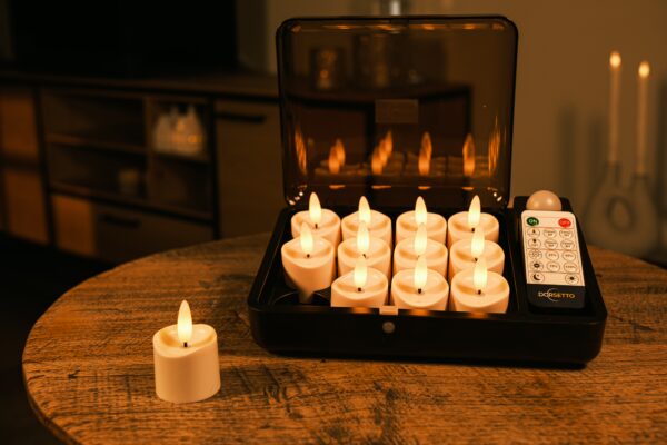 Ein Set von zwölf flammenlosen LED-Teelichtern in einer schwarzen Aufbewahrungsbox mit Fernbedienung, die auf einem Holztisch steht. Ein zusätzliches Teelicht befindet sich außerhalb des Koffers.