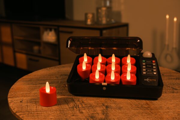 Twaalf LED-kaarsjes rood oplaadbaar 175 uur - waterdicht- met afstandsbediening (12 stuks) staan op te laden in een zwarte case op een houten tafel, één rode kaars ligt uit elkaar. De sfeervolle woonkamer is dim verlicht.