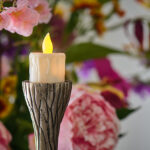 Zes oplaadbare LED-theelichtjes met kaarsvetlook, gele gloeiende vlammen en sierlijke zilveren houders voegen charme toe aan elke kamer; levendige roze en paarse bloemen creëren een zacht wazige achtergrond.