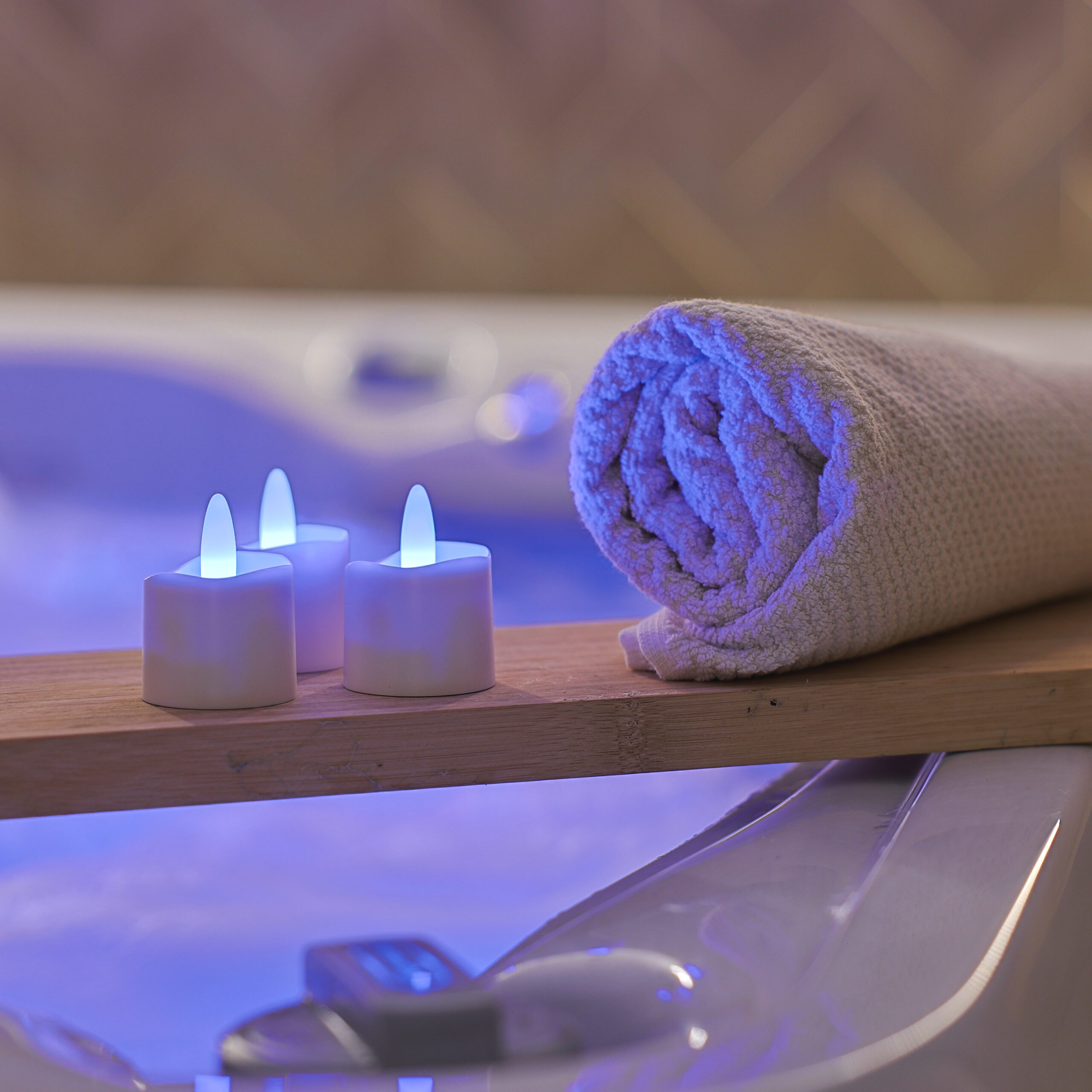 Een opgerolde handdoek en RGB led Waxinelichtje op batterij oplaadbaar waterdicht (12 stuks) met afstandsbediening rusten op een houten plank boven de jacuzzi en creëren een ontspannen spa-gevoel met zachte, kleurrijke verlichting.