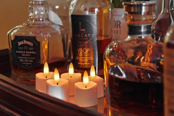 Een close-up van verschillende likeurflessen, waaronder Jack Daniel's en Lecat Cognac, opgesteld op een dienblad met vijf 3D oplaadbare LED-thee/waxinelichtjes 175 uur (met Afstandsbediening, timerfunctie) ervoor gloeiend.
