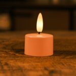 Het Oplaadbaar waxinelichtje 175 uur in blush roze straalt een warm wit licht uit met een realistisch vlameffect, dat een gezellige sfeer creëert op het houten oppervlak.