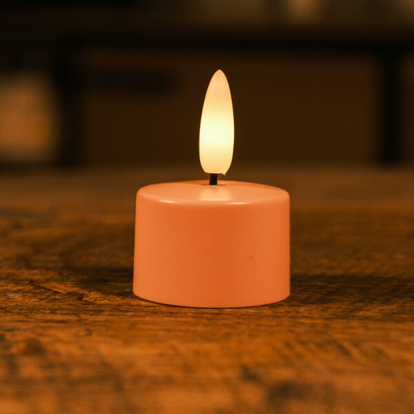 Het Oplaadbaar waxinelichtje 175 uur in blush roze straalt een warm wit licht uit met een realistisch vlameffect, dat een gezellige sfeer creëert op het houten oppervlak.