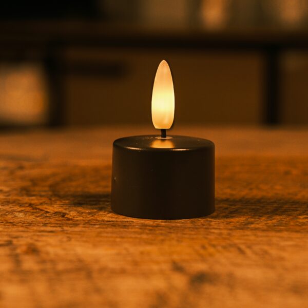 Een klein, op batterijen werkend LED waxinelichtje met een geeloranje vlam staat op een houten oppervlak en verlicht zachtjes de omgeving.