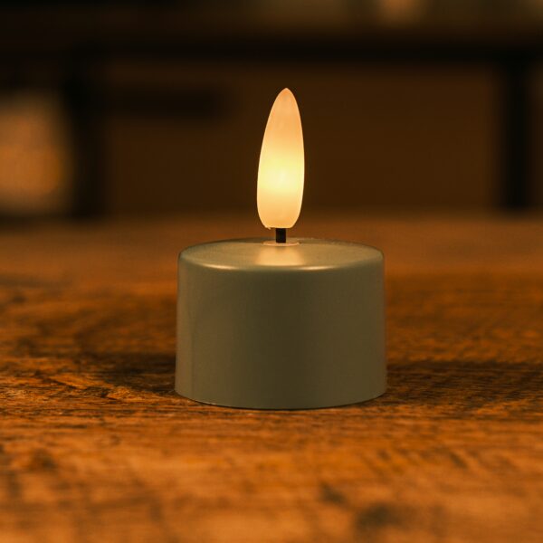 Een klein, op batterijen werkend LED waxinelichtje met een warme gele vlam staat op een houten oppervlak en creëert een gezellige sfeer.