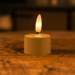 Een kleine LED-kaars op batterijen met een warme, gloeiende vlam staat op een houten oppervlak en creรซert een gezellige sfeer met zachte verlichting.