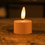 Een kleine LED-kaars op batterijen met een warme gele vlam staat op een houten oppervlak en creรซert een gezellige sfeer.
