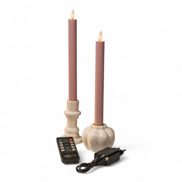 Home 17 Twee roze kaarsen op batterijen in witte houders, een afstandsbediening en een zwarte voedingsadapter staan op een witte achtergrond. De kaarsen hebben vlamvormige uiteinden die echte vlammen simuleren.