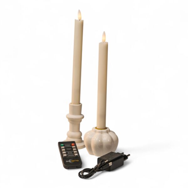 Home 16 Twee crèmekleurige LED conische kaarsen in witte houders worden afgebeeld met een zwarte afstandsbediening en een voedingsadapter, alles op een witte achtergrond. De kaarsen hebben een realistisch vlameffect.