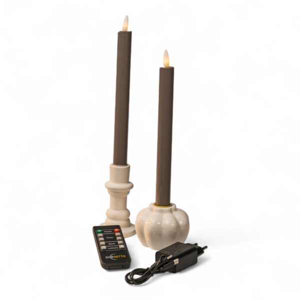 Home 19 Twee bruine vlamloze kaarsen in witte houders, vergezeld van een zwarte afstandsbediening en een stroomadapter, worden weergegeven tegen een effen witte achtergrond.