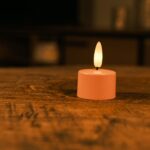 Een set van 12 oplaadbare waxinelichtjes roze met zachte, gele LED-vlam en afstandsbediening staat op een houten tafel. Elk theelichtje brandt tot 400 uur en zorgt voor sfeervolle verlichting in huis.