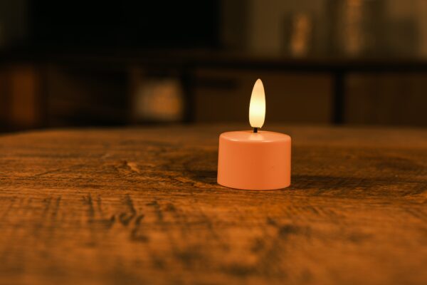 Een set van 12 oplaadbare waxinelichtjes roze met zachte, gele LED-vlam en afstandsbediening staat op een houten tafel. Elk theelichtje brandt tot 400 uur en zorgt voor sfeervolle verlichting in huis.