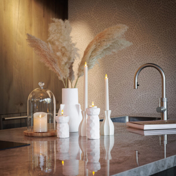 Auf einer modernen Küchentheke sorgen weiße Vasen mit Pampasgras, gestapelte Bücher, eine Kerze unter einer Glascloche und LED-Teelichter 3D (wiederaufladbar, bis zu 400 Stunden Brenndauer, Fernbedienung & Timer, 6er-Pack) in skulpturalen Halterungen für eine gemütliche, stilvolle Atmosphäre.