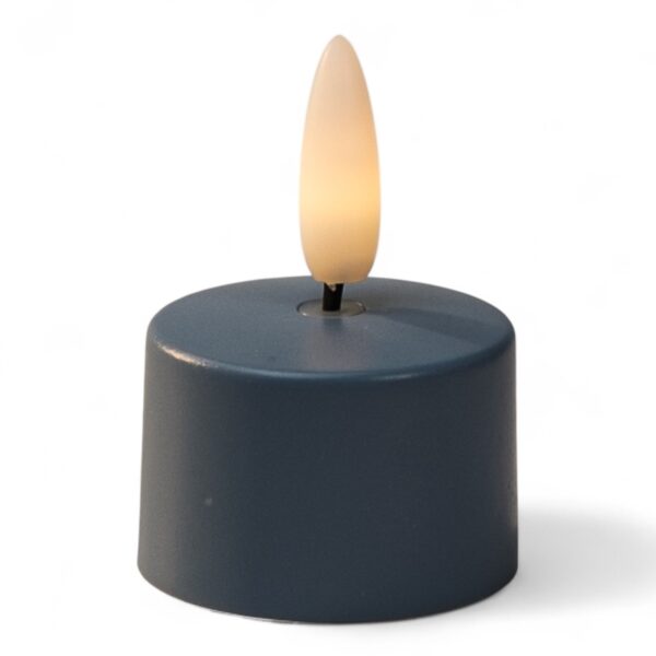 Een klein, rond, donkergekleurd LED waxinelichtje met een plastic vlamvormig topje, aangestoken om op een echte kaars te lijken, tegen een witte achtergrond.