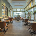 Der lichtdurchflutete Restaurantbereich mit Holzböden, braunen Stühlen und Tischen für zwei Personen ist mit LED-Lichtern wiederaufladbar mit Fernbedienung - wasserdicht - bis zu 400 Stunden Brenndauer an jedem Tisch ausgestattet, um eine gemütliche, moderne Atmosphäre zu schaffen.