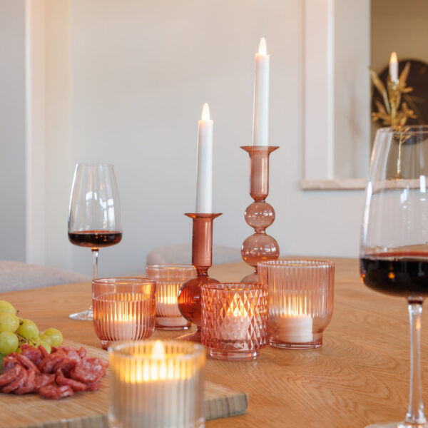 Ein Holztisch mit wiederaufladbaren LED-Teelichtern (12 Stück, warmweiß), die in rosafarbenen Glashaltern neben Wein und Wurstwaren leuchten, schafft eine gemütliche, elegante Atmosphäre; jedes Teelicht hält bis zu 400 Stunden und lässt sich einfach per Fernbedienung steuern.