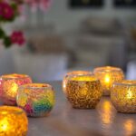 Auf einem Tisch neu arrangiert, erzeugen LED-Teelichter wiederaufladbar mit Fernbedienung ein warmes, gemütliches Licht. Im Hintergrund sorgen bunte Blumen für dekorative Akzente in dieser einladenden Szene.