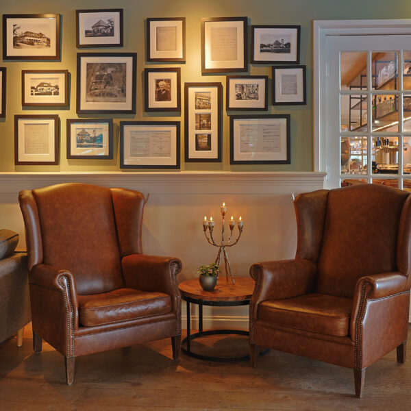 Zwei braune Ledersessel stehen vor einem kleinen runden Tisch mit einer Pflanze und LED-Teelichtern 3D (6er-Set, wiederaufladbar, bis zu 400 Stunden Brenndauer, Fernbedienung und Timer), die vor einer mit Fotos geschmückten Wand in einem gemütlichen, warm beleuchteten Raum stehen.