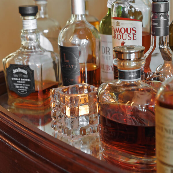 Ein Set aus verschiedenen Spirituosenflaschen und einem verspiegelten Holztablett ist mit einem strukturierten Halter dekoriert, der anstelle einer echten Kerze ein warmweißes, wiederaufladbares LED-Teelicht (bis zu 400 Stunden, 12er-Pack, Fernbedienung) enthält.