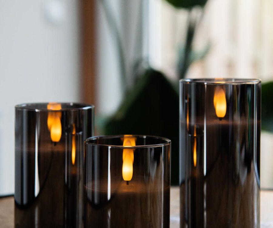 Three DORSETTO oplaadbare kaars in glas met 3D vlam staan op een houten oppervlak, hun sfeervolle licht weerkaatst in het glas. Op de achtergrond zorgen planten en daglicht voor de perfecte sfeer. Inclusief afstandsbediening, tot 105 uur brandtijd.